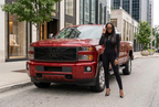 Red Chevy Silverado with a Black Widow spiderweb grille and a woman in sunglasses beside the truck on a city street.