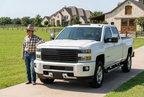White Chevy Silverado with a black American flag grille and a cowboy beside the hood at a luxury ranch.