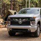 Silver pickup with an American eagle black mesh grille and stainless steel accents, parked beside a tent at a woodland campsite.